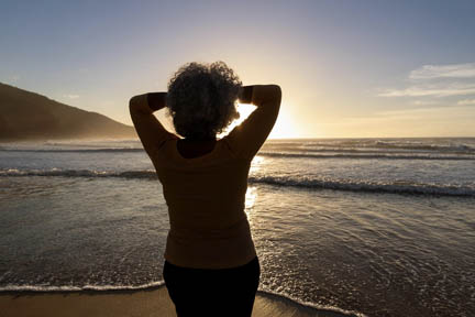 Image of the back of a woman in silhouette looking at the ocean.