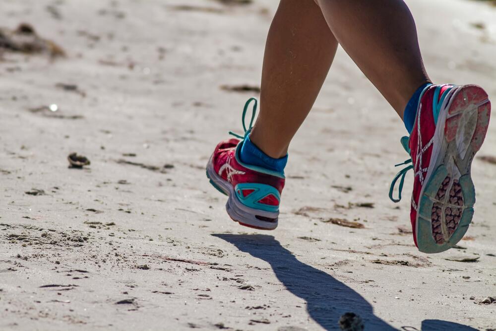 close-up of a runner's shoes and lower legs on a beach. Photo by Dulcey Lima on Unsplash.